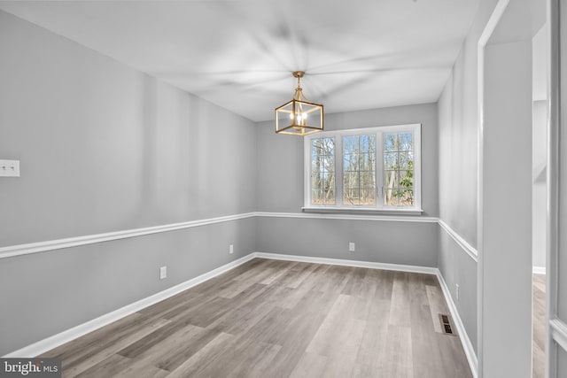 unfurnished dining area featuring a notable chandelier, baseboards, visible vents, and wood finished floors