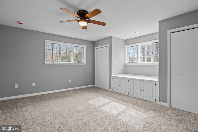 unfurnished bedroom with carpet floors, multiple windows, baseboards, and two closets