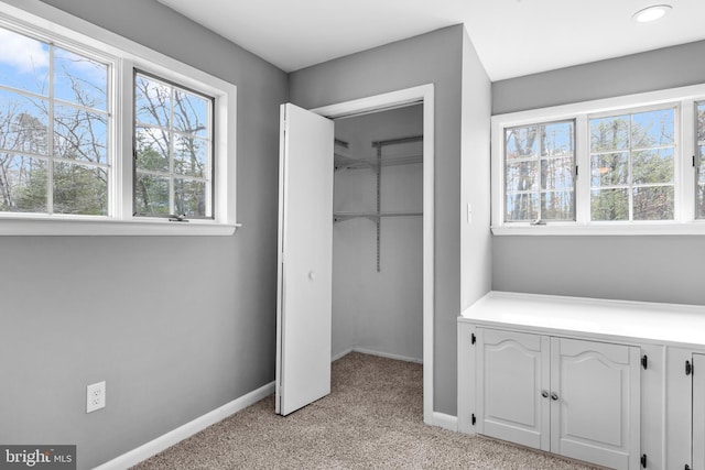 unfurnished bedroom featuring baseboards, a spacious closet, a closet, and light colored carpet