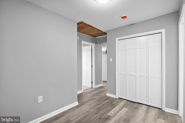 unfurnished bedroom featuring a closet, wood finished floors, attic access, and baseboards