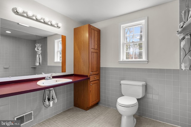 bathroom with tile patterned flooring, plenty of natural light, visible vents, and tile walls