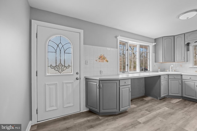 kitchen featuring a sink, gray cabinets, light countertops, light wood-type flooring, and backsplash