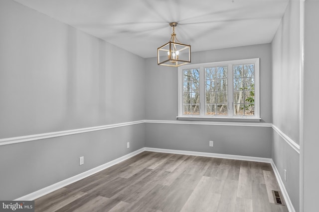 unfurnished dining area with an inviting chandelier, visible vents, baseboards, and wood finished floors