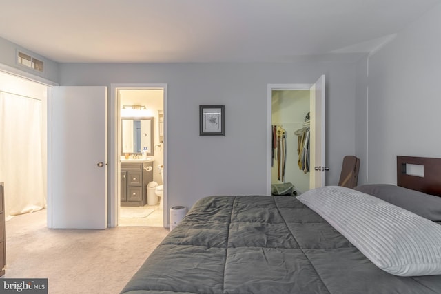 bedroom with visible vents, light colored carpet, ensuite bath, a walk in closet, and a closet