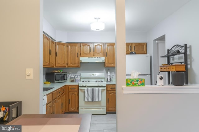 kitchen with brown cabinets, light wood finished floors, light countertops, white appliances, and under cabinet range hood