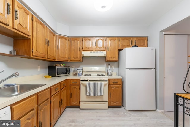 kitchen featuring light wood-style flooring, under cabinet range hood, white appliances, a sink, and light countertops