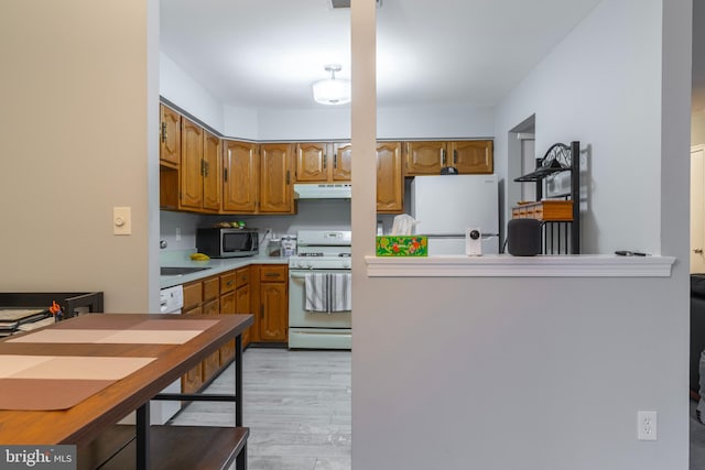 kitchen with brown cabinets, light countertops, light wood-type flooring, white appliances, and under cabinet range hood