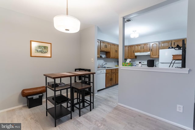 kitchen featuring white appliances, light wood-style flooring, under cabinet range hood, and light countertops