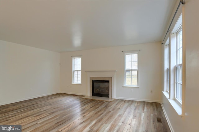 unfurnished living room featuring light wood-style flooring, a fireplace with flush hearth, visible vents, and baseboards