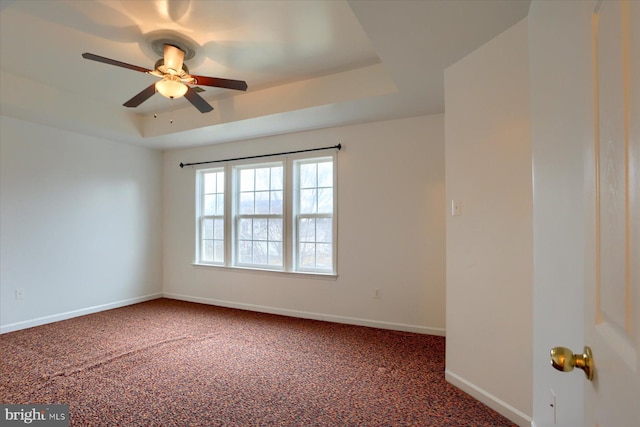 carpeted spare room with baseboards, a tray ceiling, and a ceiling fan