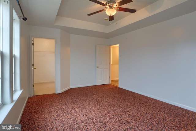 unfurnished bedroom featuring carpet floors, baseboards, a spacious closet, a closet, and a raised ceiling