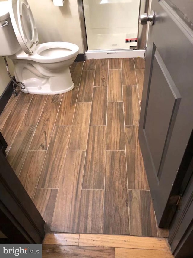 full bath with a shower stall, toilet, and wood finish floors