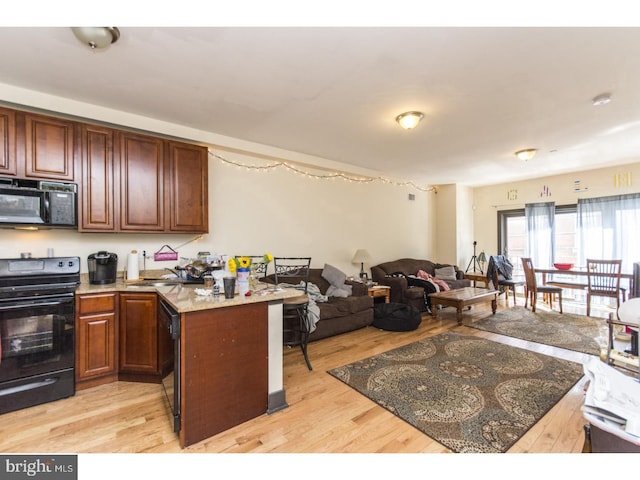 kitchen with open floor plan, a peninsula, black appliances, and light wood-style flooring