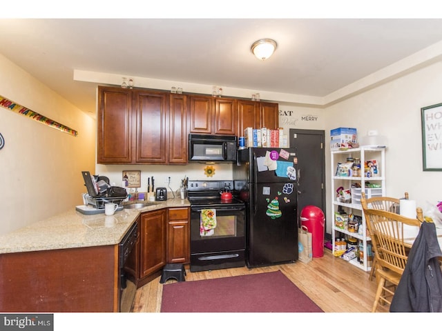 kitchen with black appliances, light wood-style flooring, light stone counters, a sink, and a peninsula