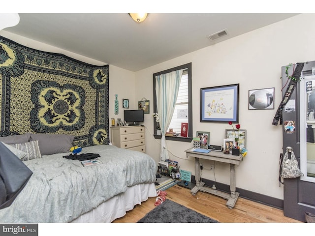 bedroom with wood finished floors, visible vents, and baseboards