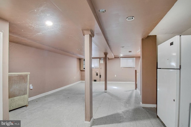 basement with light floors, baseboards, and freestanding refrigerator