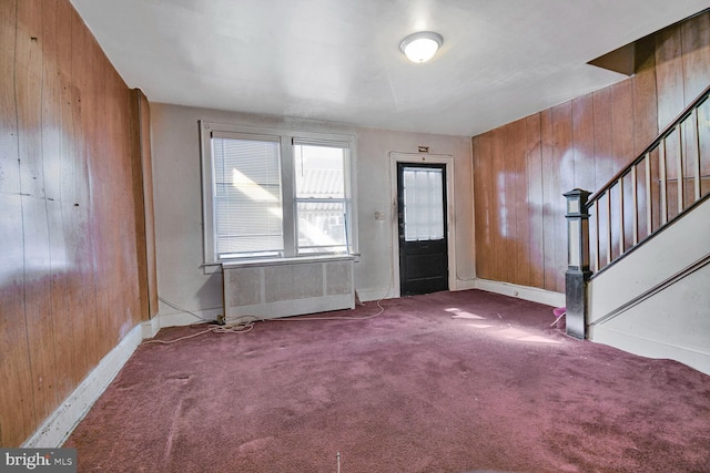 carpeted entrance foyer featuring wood walls, radiator heating unit, stairs, and baseboards