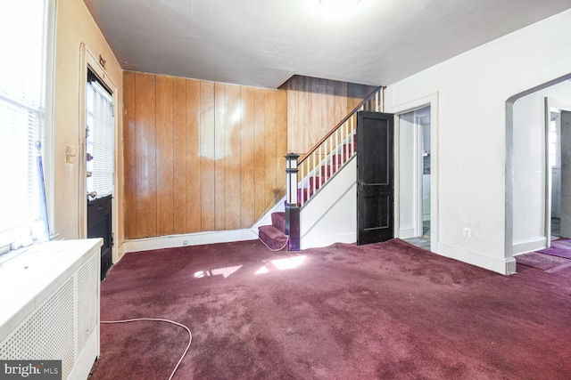 foyer entrance with wood walls, carpet flooring, baseboards, stairway, and radiator heating unit