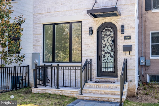 doorway to property featuring brick siding and fence