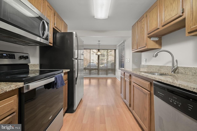 kitchen with light stone counters, light wood finished floors, appliances with stainless steel finishes, brown cabinetry, and a sink