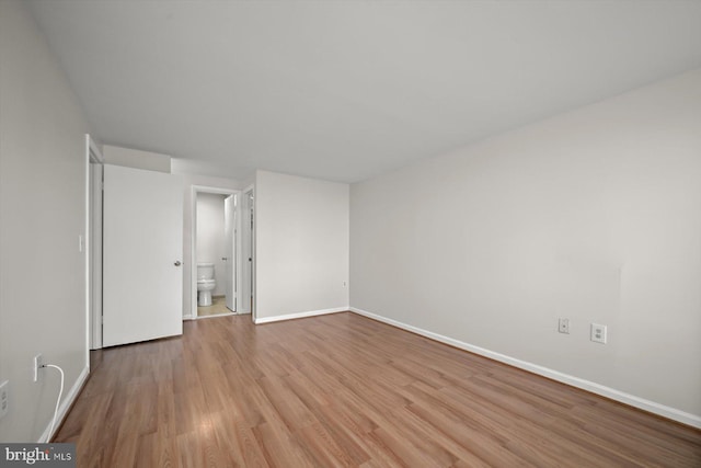 unfurnished bedroom featuring connected bathroom, baseboards, and wood finished floors