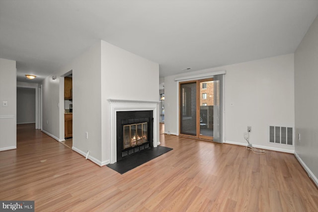 unfurnished living room featuring light wood-type flooring, a glass covered fireplace, visible vents, and baseboards