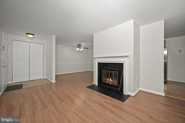 unfurnished living room with a fireplace with flush hearth, baseboards, ceiling fan, and wood finished floors