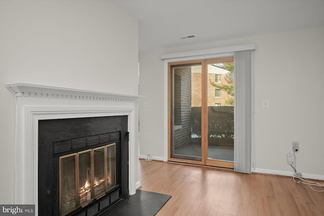 interior space featuring a glass covered fireplace, visible vents, baseboards, and wood finished floors