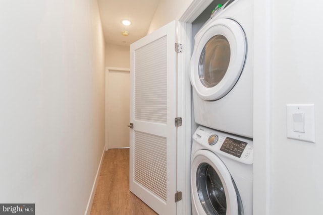 washroom featuring stacked washer and dryer, laundry area, light wood-style flooring, and baseboards