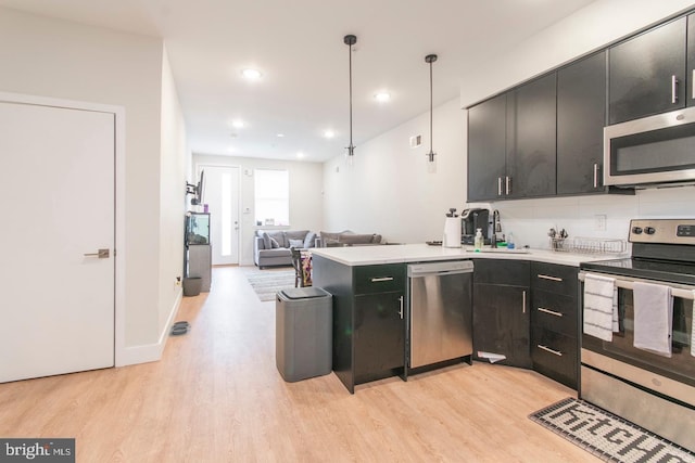 kitchen with appliances with stainless steel finishes, light wood-type flooring, dark cabinetry, and a sink