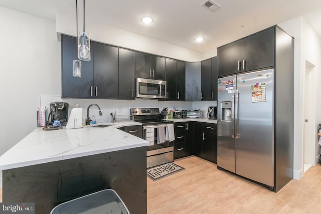 kitchen with dark cabinets, a peninsula, light stone countertops, stainless steel appliances, and a sink