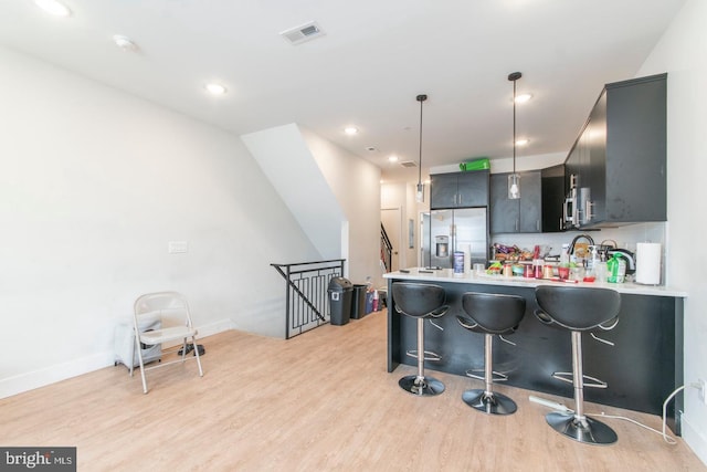 kitchen with light countertops, visible vents, light wood-style floors, stainless steel fridge, and a peninsula