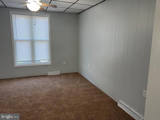 carpeted empty room featuring a paneled ceiling, a baseboard radiator, visible vents, and ceiling fan