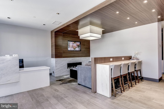 kitchen with baseboards, a high end fireplace, a kitchen breakfast bar, wood finish floors, and recessed lighting