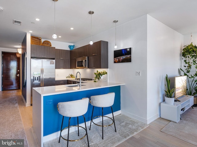 kitchen with visible vents, light wood-style flooring, appliances with stainless steel finishes, a peninsula, and a sink