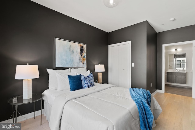 bedroom featuring light wood-style flooring, a closet, baseboards, and connected bathroom