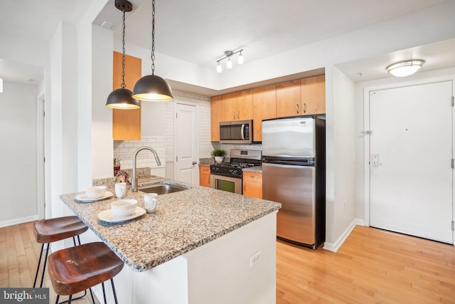 kitchen with light wood-style flooring, stainless steel appliances, a sink, and a kitchen breakfast bar