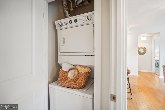 laundry area featuring light wood-style floors, stacked washer and clothes dryer, baseboards, and laundry area