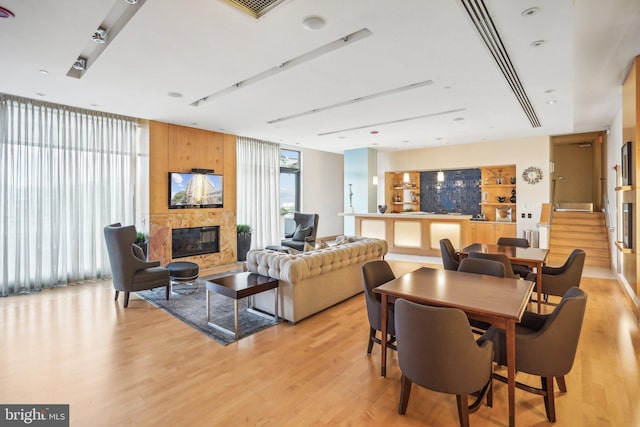 dining space with a large fireplace, a wall of windows, stairs, and light wood-style floors