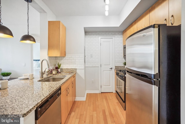 kitchen featuring light wood-style flooring, a peninsula, a sink, appliances with stainless steel finishes, and backsplash