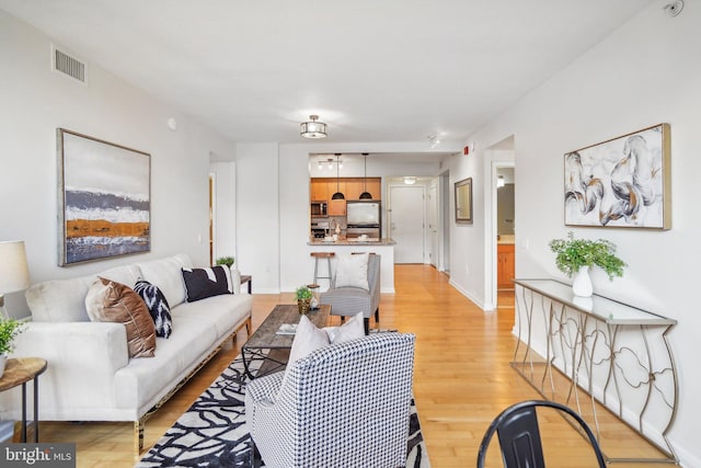 living room with light wood-type flooring, visible vents, and baseboards