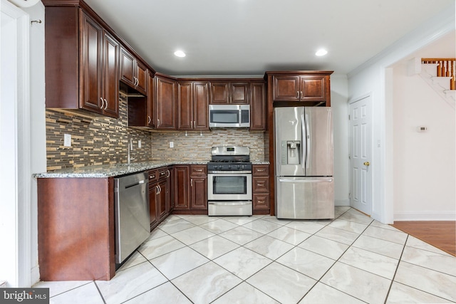 kitchen with light tile patterned floors, stainless steel appliances, baseboards, backsplash, and light stone countertops