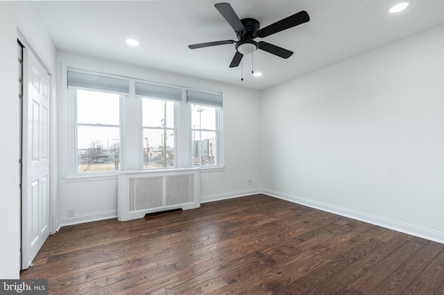 empty room featuring dark wood-type flooring, radiator heating unit, and baseboards