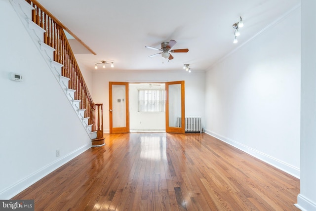 entryway with radiator, wood-type flooring, track lighting, baseboards, and stairs