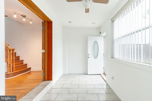 tiled entryway featuring ceiling fan, baseboards, and stairs