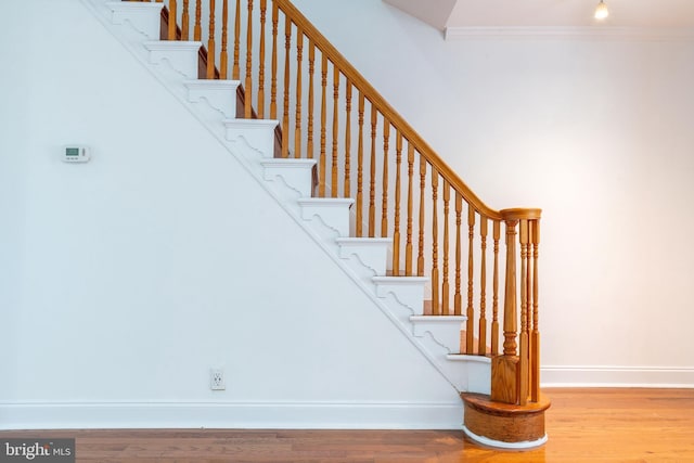 stairway featuring crown molding, wood finished floors, and baseboards