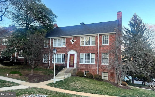 view of front facade featuring a front yard, brick siding, and a chimney