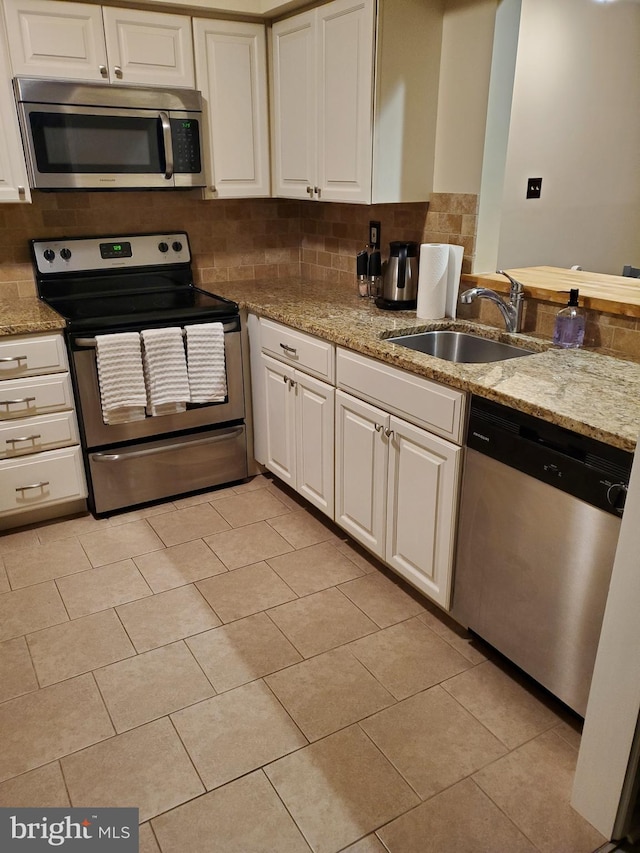 kitchen featuring a sink, light stone counters, backsplash, white cabinetry, and stainless steel appliances