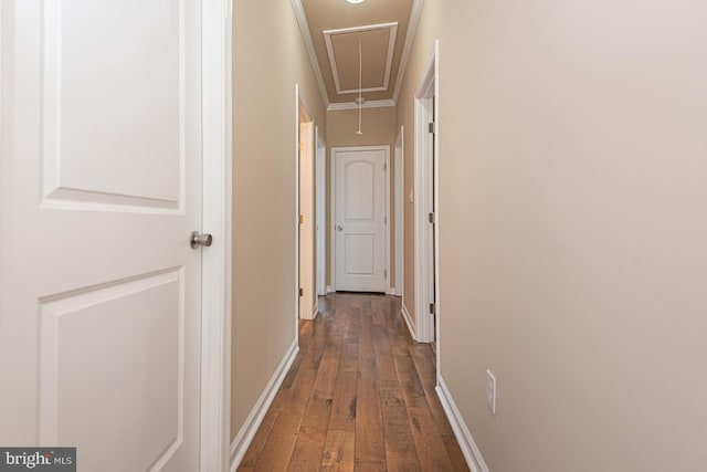 corridor with attic access, dark wood-type flooring, baseboards, and ornamental molding