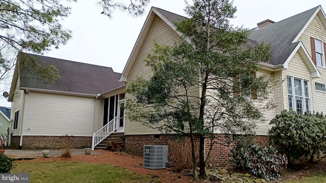 view of side of home featuring entry steps, roof with shingles, a chimney, and cooling unit